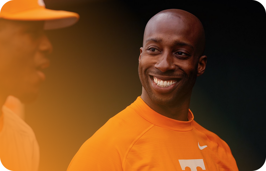 Smiling bald man in orange Tennessee Volunteers Nike shirt against dark background