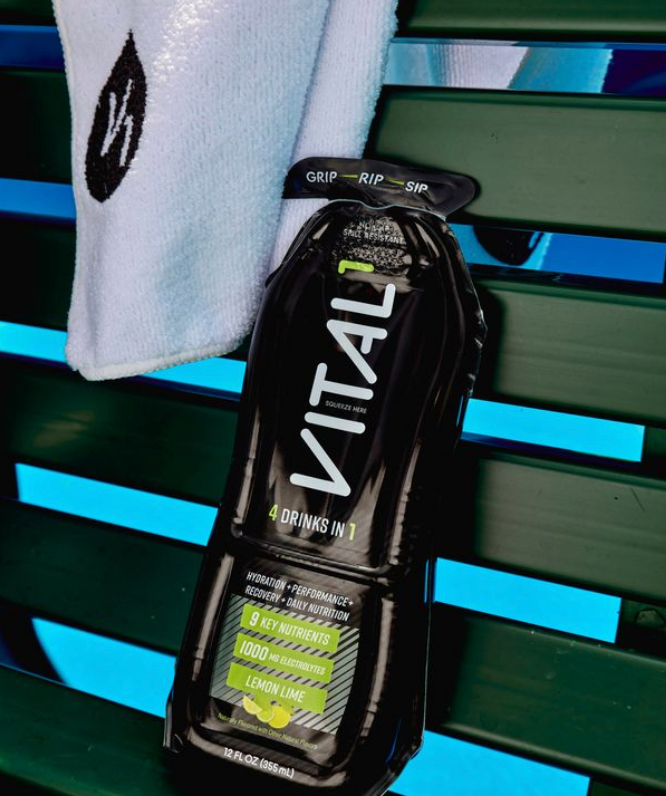 Black VITAL "4 Drinks in 1" Lemon Lime sports drink bottle with 1000mg electrolytes on green bench beside white towel